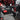 A person in a red and black plaid jacket uses a ShopVac cordless carpet cleaner with a flexible hose to clean a car interior floor mat.
